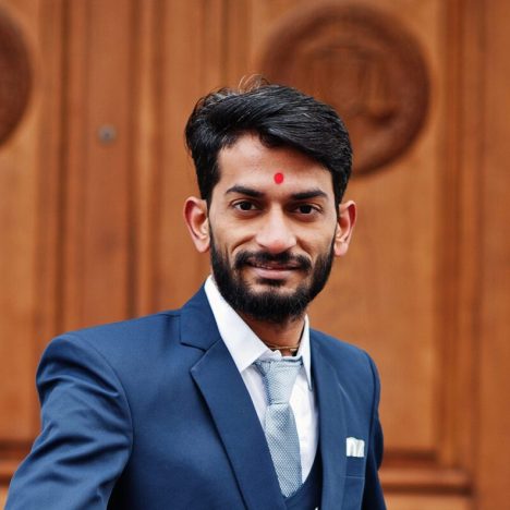 Stylish beard indian man with bindi on forehead, wear on blue suit posed outdoor against door of building.