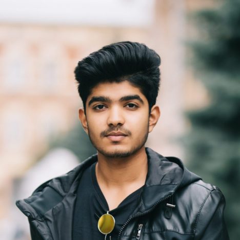 Young indian man monitoring information from social networks via cellphone connecting to 4G internet while enjoying coffee to go strolling on the street.